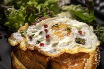Fried egg on brioche served on tray with fresh lettuce for appetizing breakfast on black background — Stock Photo
