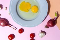 Вид сверху на сырые яйца на тарелке на яичной скорлупе и свежие веточки петрушки на двухцветном фоне — стоковое фото