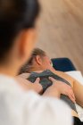 De dessus recadrée masseuse méconnaissable souriant et massant dos de la femme tout en travaillant dans une clinique de physiothérapie — Photo de stock