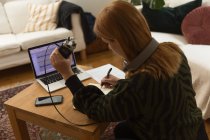 Side view of focused female radio host with mic and headphones writing in notepad while preparing for recording podcast at home — Stock Photo