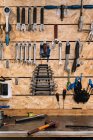 Varias herramientas de metal colgando en filas en la pared de madera en servicio de reparación de bicicletas en mal estado - foto de stock