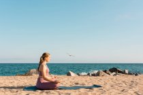 Смирна жінка сидить у Падмасані і робить йогу, роздумуючи з закритими очима на піщане узбережжя. — стокове фото