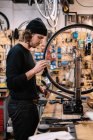 Vue latérale du jeune maître mâle examinant le pneu sur la roue du vélo tout en travaillant dans un atelier de service de réparation professionnel — Photo de stock