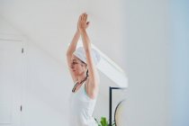 Femme debout dans Vrksasana pose tout en pratiquant le yoga sur tapis doux et regardant loin dans la chambre de la maison — Photo de stock
