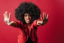 Verängstigte Afroamerikanerin mit lockigem Haar zeigt Stopp-Geste auf rotem Hintergrund im Studio und blickt in die Kamera — Stockfoto