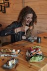 Lächelnde Frau isst schmackhaftes Sushi in japanischem Restaurant, während sie am Holztisch sitzt — Stockfoto