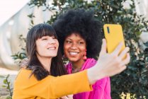 Delighted multiracial LGBT couple of women taking self shot on smartphone in summer garden — Stock Photo