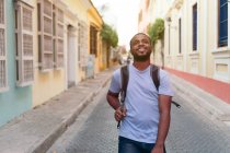 Улыбающийся африканский мужчина с рюкзаком смотрит вверх, стоя на улице — стоковое фото