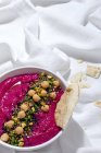 Top view of appetizing beetroot hummus garnished with chickpea served on fabric background with bread — Stock Photo