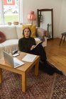 Високий кут вдумливої жінки-радіоведучої, що пише в блокноті, сидячи на підлозі вдома і записуючи подкаст — стокове фото