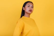 Porträt einer Asiatin, die auf gelbem Hintergrund im Studio steht und in die Kamera blickt — Stockfoto