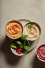 Top view of bowls with assorted hummus served on table with fresh cucumbers and radish — Stock Photo