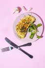 Omelette savoureuse sur assiette contre les brins de persil frais avec gousses d'ail sur fond rose — Photo de stock