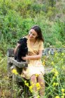 Fröhliche Hündin mit schwarzem, flauschigem Welpen sitzt auf Holzbank im Grünen — Stockfoto