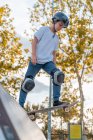 Vista laterale a basso angolo di coraggioso pattinatore adolescente in piedi sullo skateboard e che si prepara per mostrare trucco sulla rampa nello skate park — Foto stock