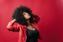 Naughty African American female screaming and touching hair on red background in studio — Stock Photo