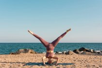 Relaxed female balancing in Salamba Sirsasana on mat while doing yoga on seashore — Stock Photo