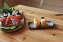 Сверху тарелка с разнообразными суши-роллами, сжигаемыми факелом обрезанным неузнаваемым поваром, подаваемым на стол в японском ресторане — стоковое фото