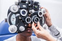 Optometrista che regola l'apparecchiatura di optometria durante lo studio della vista di una donna nera — Foto stock