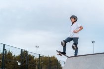 Teenage skater in protective gear riding skateboard during weekend in skate park and looking away — Stock Photo