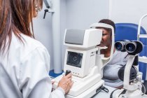 Optometrista che regola il retinografo durante lo studio della vista di una donna nera — Foto stock