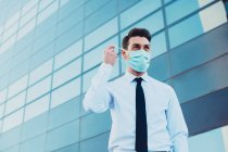 Dal basso di imprenditore maschile in abbigliamento formale con maschera medica guardando altrove in città durante la pandemia di coronavirus — Foto stock