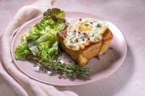 Высокий угол жареного яйца на булочке подается на тарелке со свежим салатом для аппетитного завтрака на розовом фоне — стоковое фото