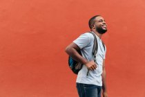 Улыбающийся черный мужчина с рюкзаком смотрит вверх, стоя на улице — стоковое фото