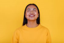 Delighted Asian female standing on yellow background in studio with eyes closed — Stock Photo