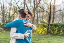 Alegre LGBT casal de machos abraçando enquanto de pé no parque no ensolarado dia — Fotografia de Stock