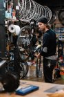 Вид сбоку серьезного мужского механического ремонтного колеса велосипеда во время работы в мастерской — стоковое фото