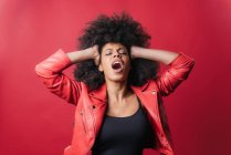 Freche Afroamerikanerin schreit und berührt Haare auf rotem Hintergrund im Studio — Stockfoto
