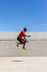 Vista lateral do atleta masculino afro-americano enérgico pulando corda acima do solo enquanto faz exercícios durante o treinamento no verão — Fotografia de Stock