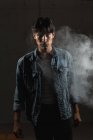 Porträt eines jungen lateinischen Mannes, der selbstbewusst in die Kamera blickt, inmitten von Rauch unter dramatischem Licht — Stockfoto