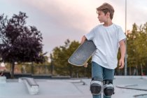 Adolescente em equipamento de proteção de pé com skate no parque de skate e olhando para longe — Fotografia de Stock