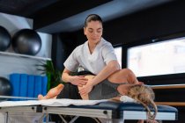 Terapeuta femenina en bata blanca masajeando la espalda de la mujer durante la sesión de osteopatía en la clínica - foto de stock