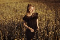 Retrato de uma bela jovem mulher com no campo olhando para longe entre as flores — Fotografia de Stock
