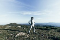 Full body self assured male astronaut in spacesuit and helmet holding hands on waist while standing on grass and stones in highlands — Stock Photo