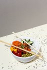 De dessus baguettes de bambou placé sur le dessus du bol avec plat poke savoureux sur la table couverte de graines de sésame — Photo de stock