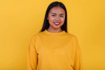 Delighted Asian female standing on yellow background in studio while looking at camera — Stock Photo