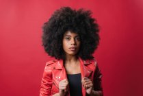 Восхитительная афроамериканка с прической Афро, смотрящая на камеру на красном фоне в студии — стоковое фото