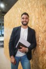 Delizioso imprenditore maschio con documenti in piedi vicino al muro in moderno spazio di coworking e guardando la fotocamera — Foto stock