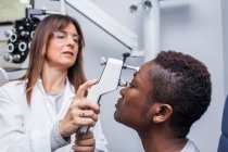Optometrista che utilizza un oftalmoscopio durante lo studio della vista di una donna nera — Foto stock