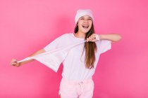 Беззаботные женщины-подростки в повседневной одежде с каштановыми волосами и платком, представляющие концепцию осознания, отводя взгляд, стоя на розовом фоне — стоковое фото
