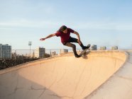 Male skateboarder riding skateboard on platform under cloudy blue sky in urban skate park on sunny day — Stock Photo