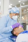 Estomatologista feminina em máscara uniforme e respiratória curando dentes de paciente do sexo masculino no hospital — Fotografia de Stock