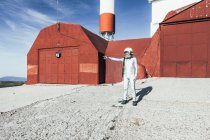Homme en combinaison spatiale debout près du mur rouge de l'installation industrielle par une journée ensoleillée — Photo de stock