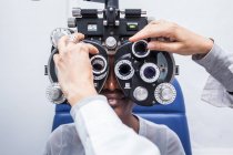 Optometrista ajustando o equipamento de optometria durante o estudo da visão de uma mulher negra — Fotografia de Stock