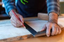 Crop adult male woodworker with pencil and ruler marking wooden board while working at workbench in carpentry workshop — Stock Photo