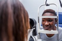 Оптометрист коригує ретинограф під час вивчення зору щасливої чорної жінки — стокове фото